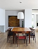 Simply wooden table and Scandinavian-style chairs below white pendant lamp in open-plan interior