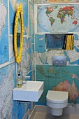Guest toilet with walls covered in maps and gilt-framed, oval mirror above modern sink