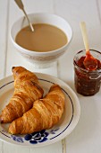 Two croissants, berry jam and a bowl of latte for breakfast