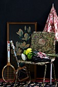 Bouquet on retro chair and tennis racquets in front of framed picture leaning on black-painted wall