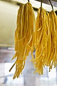 Bunches of tagliatelle hung up on large hooks to dry