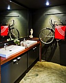 Moderne Waschtischzeile und als Handtuchhalter verwendetes, an die Wand gehängtes Fahrrad in dunkel getöntem Badezimmer
