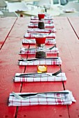 Folded red and white linen napkins, cutlery, pepper mills and salt cellars on red-painted garden table