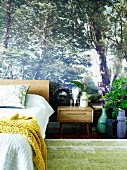 Photo wallpaper with forest motif in bedroom; matching accessories such as plant arrangements and floral print pillows