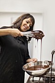 A confectioner holding an egg whisk and a metal bowl with melted chocolate