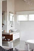 Corner washstand with framed mirror and integrated wooden shelf in pale bathroom with polished concrete floor