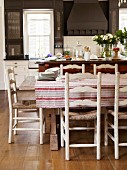 Tablecloth on rustic table and wooden, rush-bottom chairs in country-style kitchen