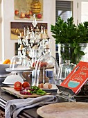 Vegetables on chopping board and various dishes with glass covers next to cookery book on kitchen counter