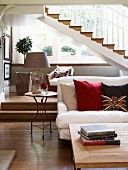 Sofa with scatter cushions and coffee table in front of platform with steps below staircase in elegant country house
