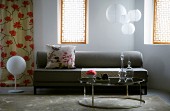 Retro-style, round side table in front of grey sofa and spherical pendant lamps between windows with Oriental-style screens