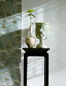 Flower in vase on black-painted plant stand next to strip of wallpaper with stylised pattern