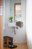 Badezimmer mit weissen Fliesen, Waschbecken, Spiegel und Holzhocker