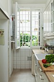 In schmaler Küche Gemüse auf Küchenzeile und stirnseitig vergittertes offenes Fenster
