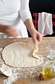 Pizza dough being stretched out on a wooden table
