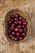 A basket of cherries on a wooden surface (view from above)