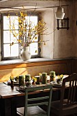 Frühlingshafter Esstisch mit Kerzen und Blumen vor Fenster, Forsythien in Porzellankrug auf Fensterbank