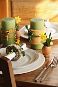 Green candles wrapped in decorative ribbons and place settings with Easter decorations on wooden table