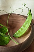 sinle mange tout bean in a wooden bowl with fresh bean leaves