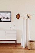 Old-fashioned hats on designer coat rack next to white sideboard with wooden frame below framed picture