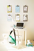 Hand-crafted clipboards on wall above small, white desk with laptop and white chair