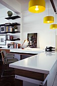 Open-plan interior with desk and adjoining kitchen counter below yellow pendant lamps