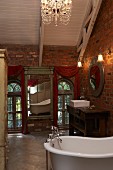 Antique mirror on wall and free-standing bathtub in romantic, vintage bathroom in attic interior with brick walls