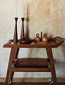 Artistic wooden vessels and candlesticks and stack of leather, patchwork table mats on serving trolley against antique, marbled wall