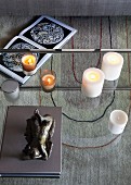 Skulptur und Kerzen auf Glastisch mit Durchblick auf das grafische Teppichmuster und ein geöffnetes Buch
