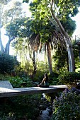 Frau bei Meditation auf Holzsteg in tropischem Garten
