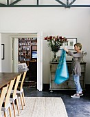 Woman in front of chest of drawers in dining area next to open double doors with view into living room