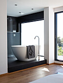 Purist ensuite bathroom with free-standing, white, designer bathtub and shower area on black platform