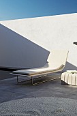 Elegante weiße Designerliege auf grauem Naturstein Terrassenbelag vor weißer sonniger Innenhofwand