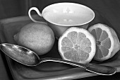 Lemons and a spoon in front of a teacup (black and white image)