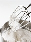 Egg whites whisked until stiff in a mixing bowl and on the whisks