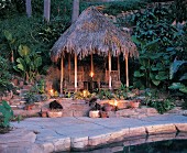 Tiki hut at pool side at dusk with candles and garden plants