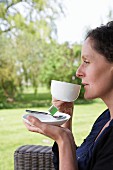 Woman drinking cup of tea on terrace in garden