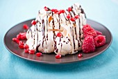 A meringue dessert with raspberries, pomegranate seeds and chocolate sauce