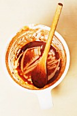 A dirty measuring jug with a wooden spoon and the remains of chocolate sauce