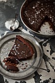 Dark chocolate truffle cake sprinkled with salt, a slice on a silver plate