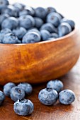Blueberries in and in front of a wooden bowl