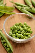 Peas in a glass bowl among pea pods