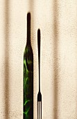 An elongated shadow of a wine bottle and a fork against the wall