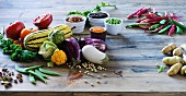 A vegetable still life featuring aubergines, pulses, squash and potatoes on a wooden table