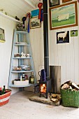 Cosy, cabin atmosphere with fire in nostalgic iron stove and light blue corner shelves in renovated shepherd's hut