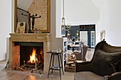 Fire burning in open fireplace in open-plan, loft-style living room with antique upholstered furniture and designer kitchen in background
