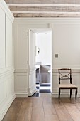 Eine in der weißen Holzvertäfelung versteckte Tür öfffnet sich zum Gästebad in einem minimalistisch elegantem Landhaus Flur