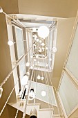 View up square stairwell with light sculpture made from various pendant lamps suspended from ceiling