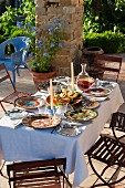 Gedeckter Gartentisch mit buntem Geschirr in sommerlicher mediterraner Stimmung