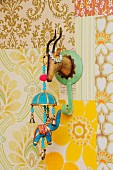 Retro ornaments in child's bedroom; Indian elephant mobile hanging from tin coat hook shaped like hunting trophy on patchwork of 70's wallpapers