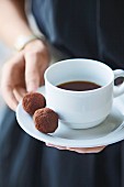 A woman holding a cup of coffee with two chocolate truffles